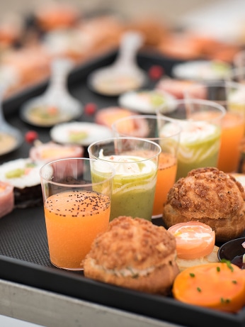 Plateau d'amuse-bouches et verrines colorées pour un cocktail. Verrines orange aux graines, vertes crémeuses, petits choux salés et bouchées variées.